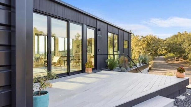 A modern building with large windows, a wooden deck, and potted plants.