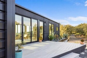 Un bâtiment moderne doté de grandes fenêtres, d’une terrasse en bois et de plantes en pot.