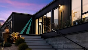 A modern building with a staircase leading to a dark entrance, surrounded by plants and a clear sky.