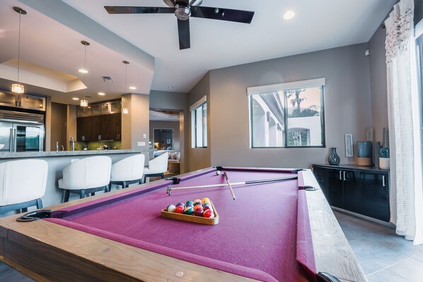 A pool table with balls, a ceiling fan, and a kitchen area with a bar.