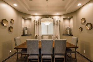 A dining room with a wooden table and six upholstered chairs, a chandelier, and decorative plates on the walls.