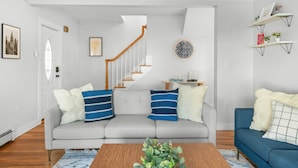Ein Wohnzimmer mit grauem Sofa, blau-weißen Kissen, einem Holztisch und einer Treppe im Hintergrund.