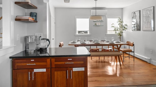 Eine moderne Küche mit Holzschränken, einer schwarzen Arbeitsplatte und einem Essbereich mit Holztisch und -stühlen.