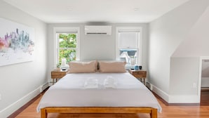 Ein modernes Schlafzimmer mit einem großen Bett, zwei Nachttischen, einer Wand-Klimaanlage und einem Stadtbild.