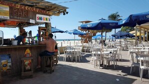 Un bar frente a la playa con mesas al aire libre y sombrillas.