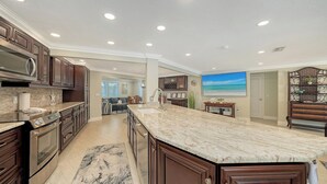 Una cocina amplia con alacenas de madera oscura, una isla grande y vistas a un salón.