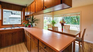 A kitchen with wooden cabinets, a large countertop, and a window overlooking a backyard.