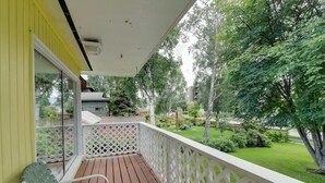 A wooden deck with a white lattice railing, a green chair, and a view of a well-maintained garden and trees.