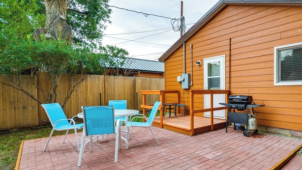 Ein Holzhaus mit einer Terrasse, komplett mit Tisch, Stühlen, einem Grill und einer Holzterrasse.
