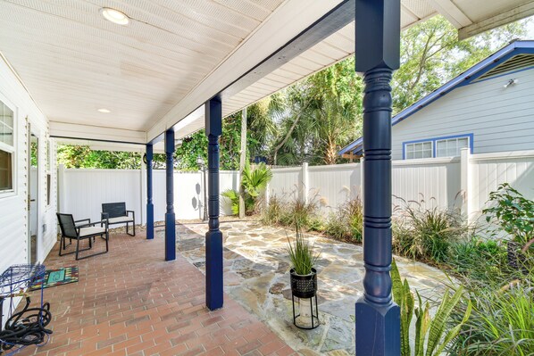 A covered patio with brick flooring, outdoor furniture, and potted plants.
