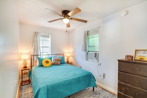 Une chambre à coucher avec un lit, un ventilateur de plafond, une commode et une fenêtre avec des rideaux.