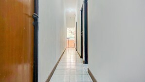 A corridor with a wooden door on the left and a black door on the right, leading to a bright room with a window. - OYO 90359 Sbh Residence (Medan)