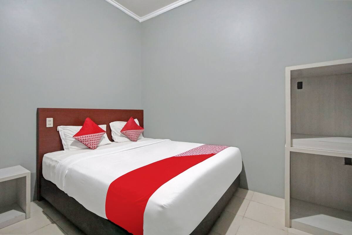 A neatly made bed with white and red bedding, a wooden headboard, and a grey wall.