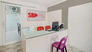 A reception desk with a glass top, red and purple chairs, a computer, and a sign reading "SBH Residence by SQUAM". - OYO 90359 Sbh Residence (Medan)