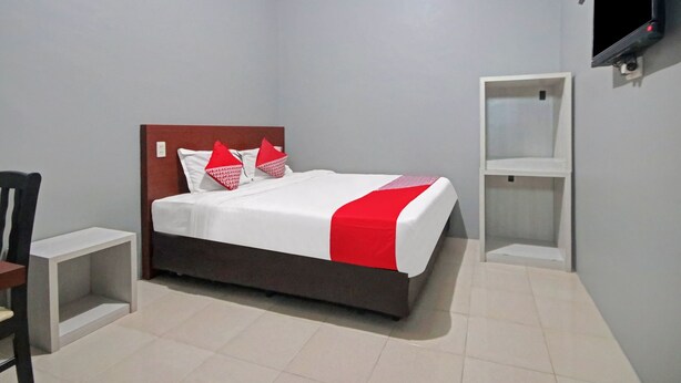 A neatly arranged hotel room with a bed, a chair, a TV, and a shelf. - OYO 90359 Sbh Residence (Medan)