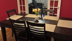 Una sala da pranzo con un tavolo in legno scuro, quattro sedie, un vaso con fiori e una lampada gialla dalla superficie strutturata.