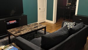Un soggiorno con pareti color verde acqua, un divano scuro, un tavolino da caffè e una TV a schermo piatto su un mobile.