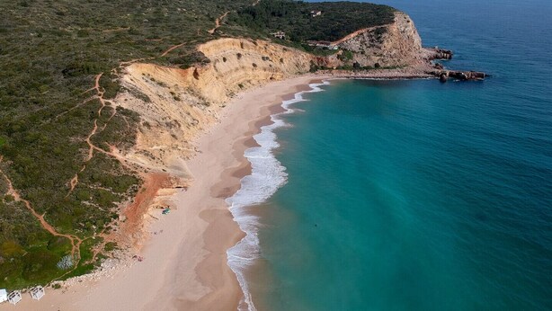 A coastal landscape with a sandy beach, a rocky cliff, and a clear view of the sea.