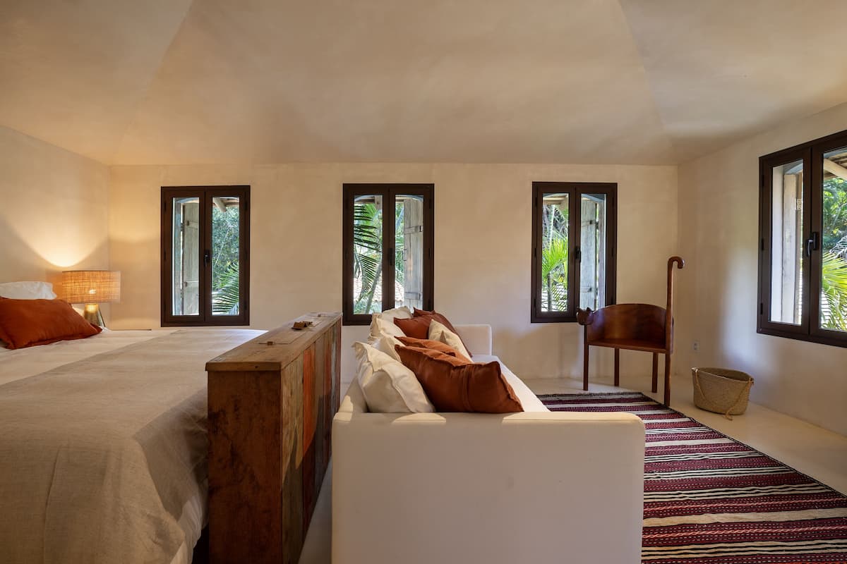 A bedroom with two beds, a wooden bench, a white sofa, and a patterned rug.