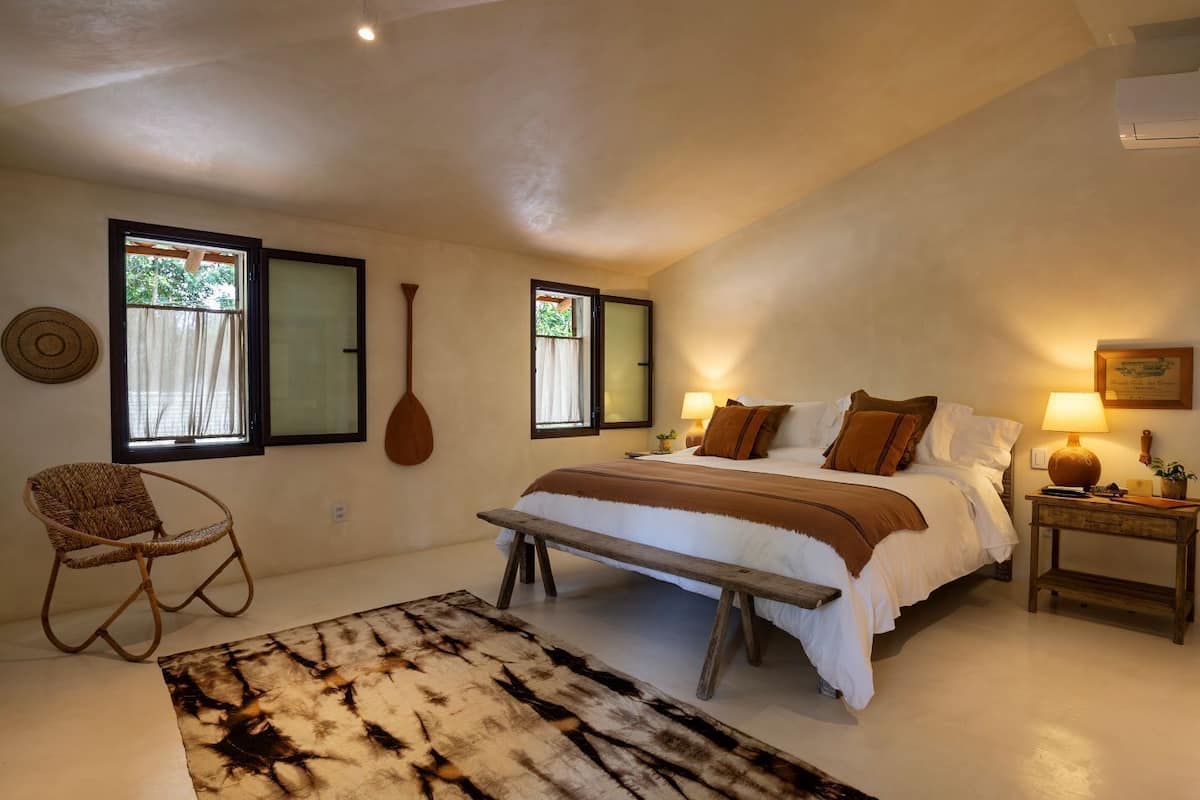 A bedroom with a bed, a wooden bench, a wicker chair, and a rug.