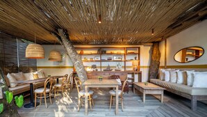 A cozy outdoor dining area with a wooden table and chairs, surrounded by a wooden deck and a thatched roof. - Na Praça Hotel (Porto Seguro)