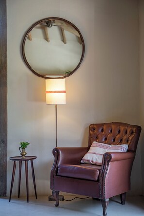 A room with a brown leather armchair, a round mirror, a floor lamp, and a small wooden table with a plant. - Na Praça Hotel (Porto Seguro)