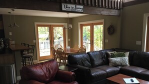Ein Wohnzimmer mit braunem Ledersofa, einem Holzesstisch mit Stühlen und einer Küchenzeile mit Bar.