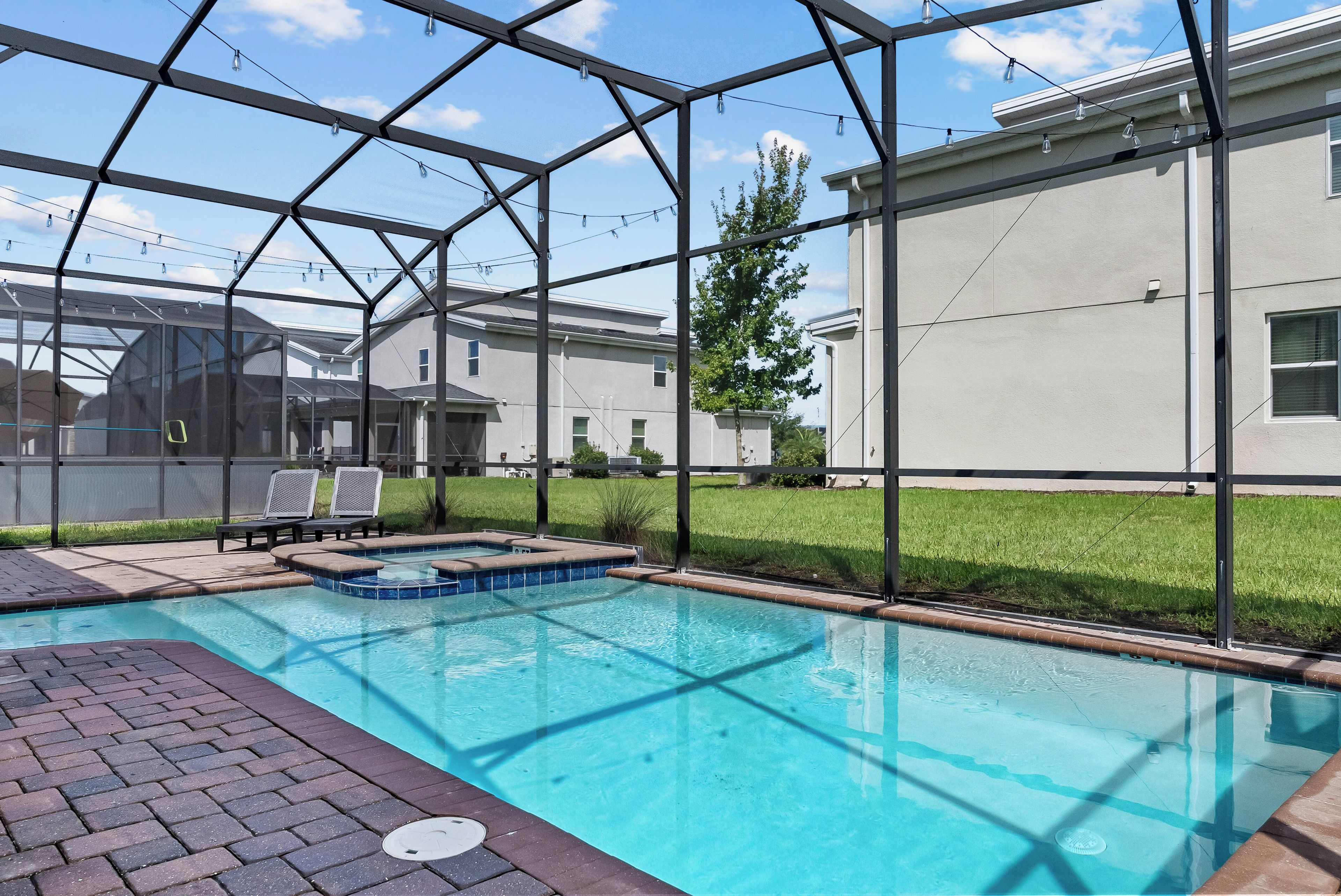 A swimming pool with a clear blue water, surrounded by a covered area with chairs and a view of a residential building.