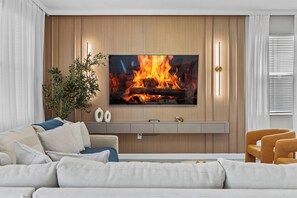 A modern living room with a flat-screen TV mounted on a wooden wall, a sofa with cushions, a side table with decorative items, and a potted plant. - New Home 8 Bedrooms and 5 Bathrooms At Storey Lake (Kissimmee)
