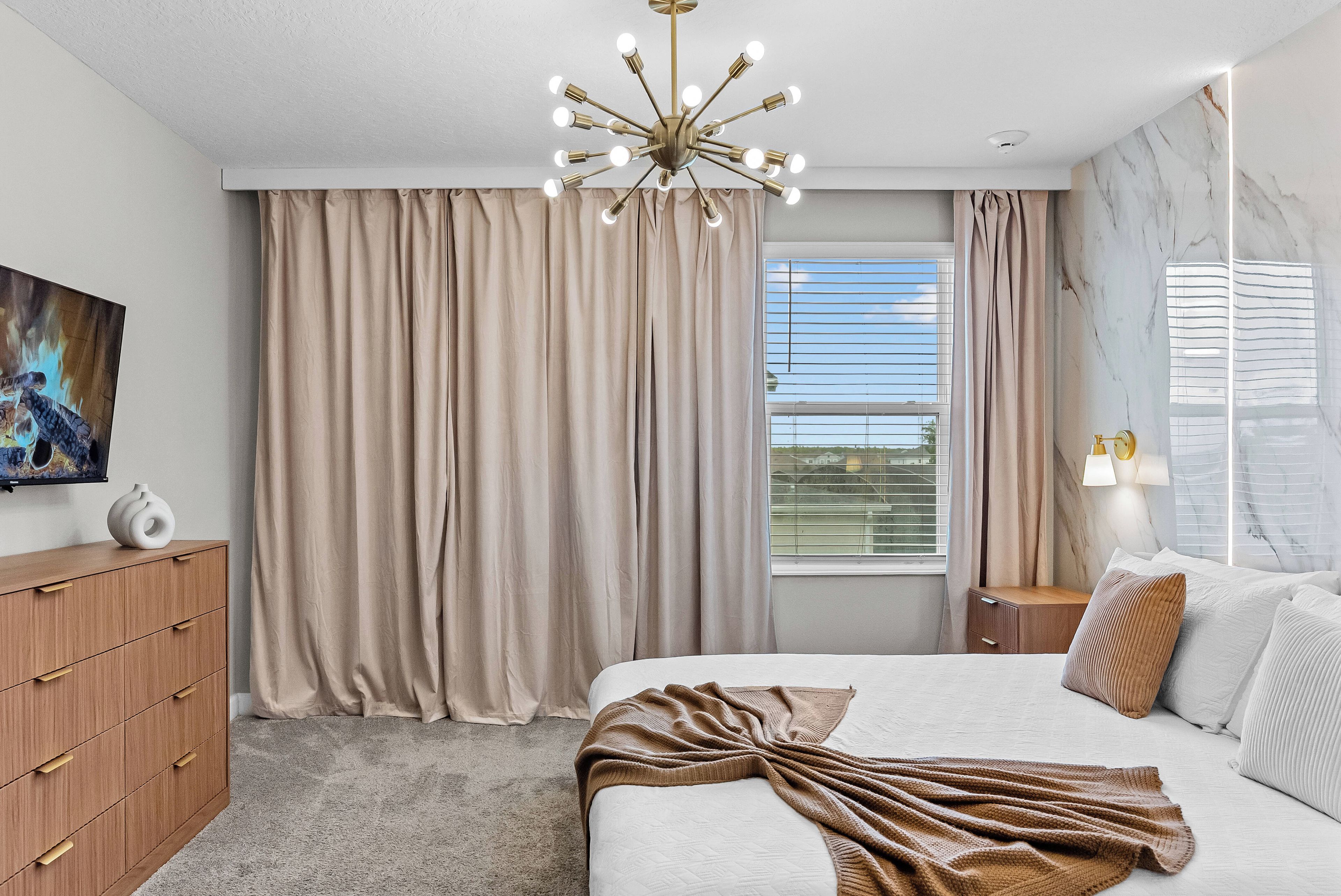 A hotel room with a bed, a wooden dresser, a painting, a window with blinds, and a marble wall.
