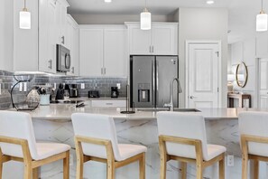 A modern kitchen with white cabinets, a stainless steel refrigerator, a coffee maker, and a marble countertop. - New Home 8 Bedrooms and 5 Bathrooms At Storey Lake (Kissimmee)