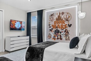 Ein modernes Schlafzimmer mit Wandkunst zum Thema Star Wars, einem Fernseher, einer weißen Kommode und einem Bett mit schwarzer Decke.