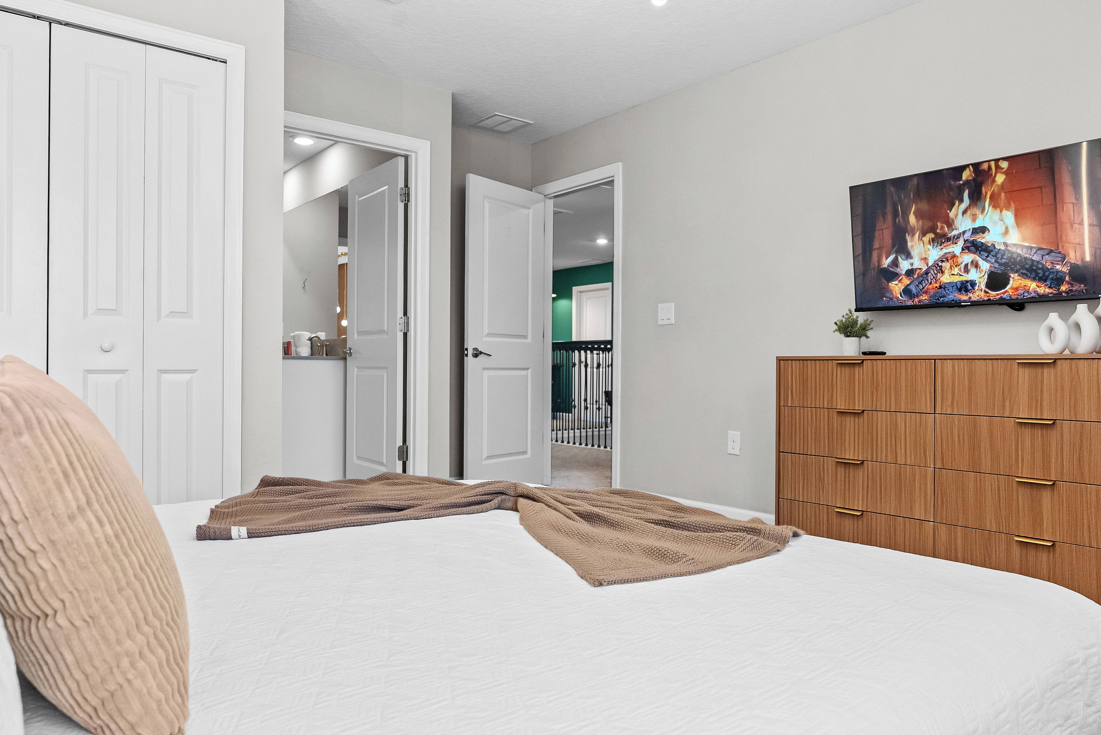 A bedroom with a bed, a wooden wardrobe, and a painting of a fire on the wall.