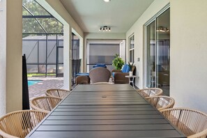Eine überdachte Terrasse mit einem langen Tisch und Korbstühlen, ein Pool im Hintergrund und ein Blick ins Freie.