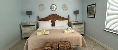 A bedroom with a bed, two nightstands, a ceiling fan, and a window with blinds.