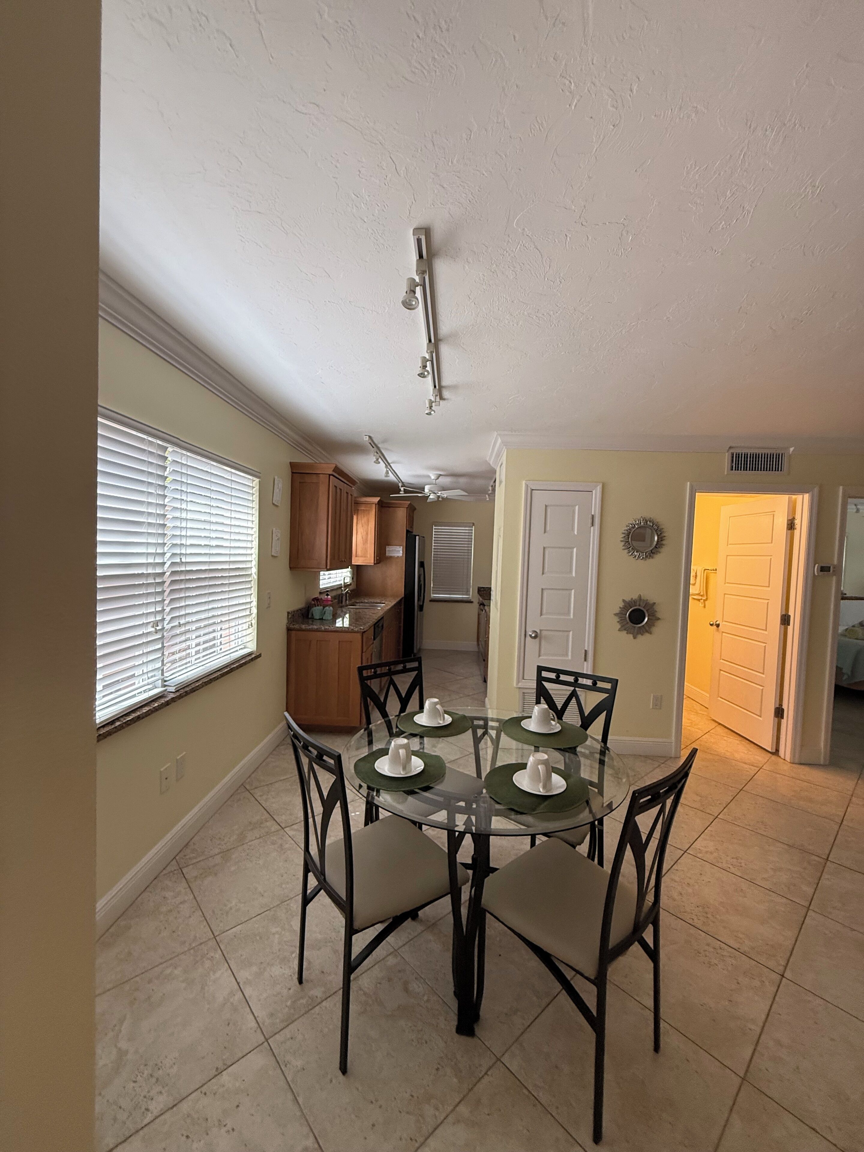 A dining area with a glass table, four chairs, and a ceiling fan.