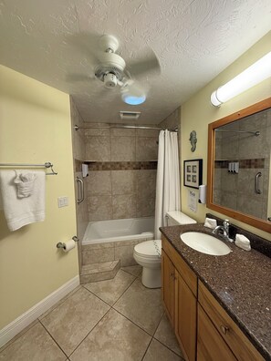 A bathroom with a bathtub, toilet, shower, and vanity with a sink and mirror.