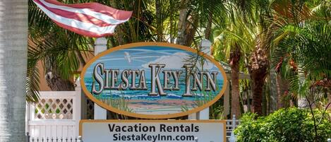 A sign for Siesta Key Inn with a beach scene and an American flag.
