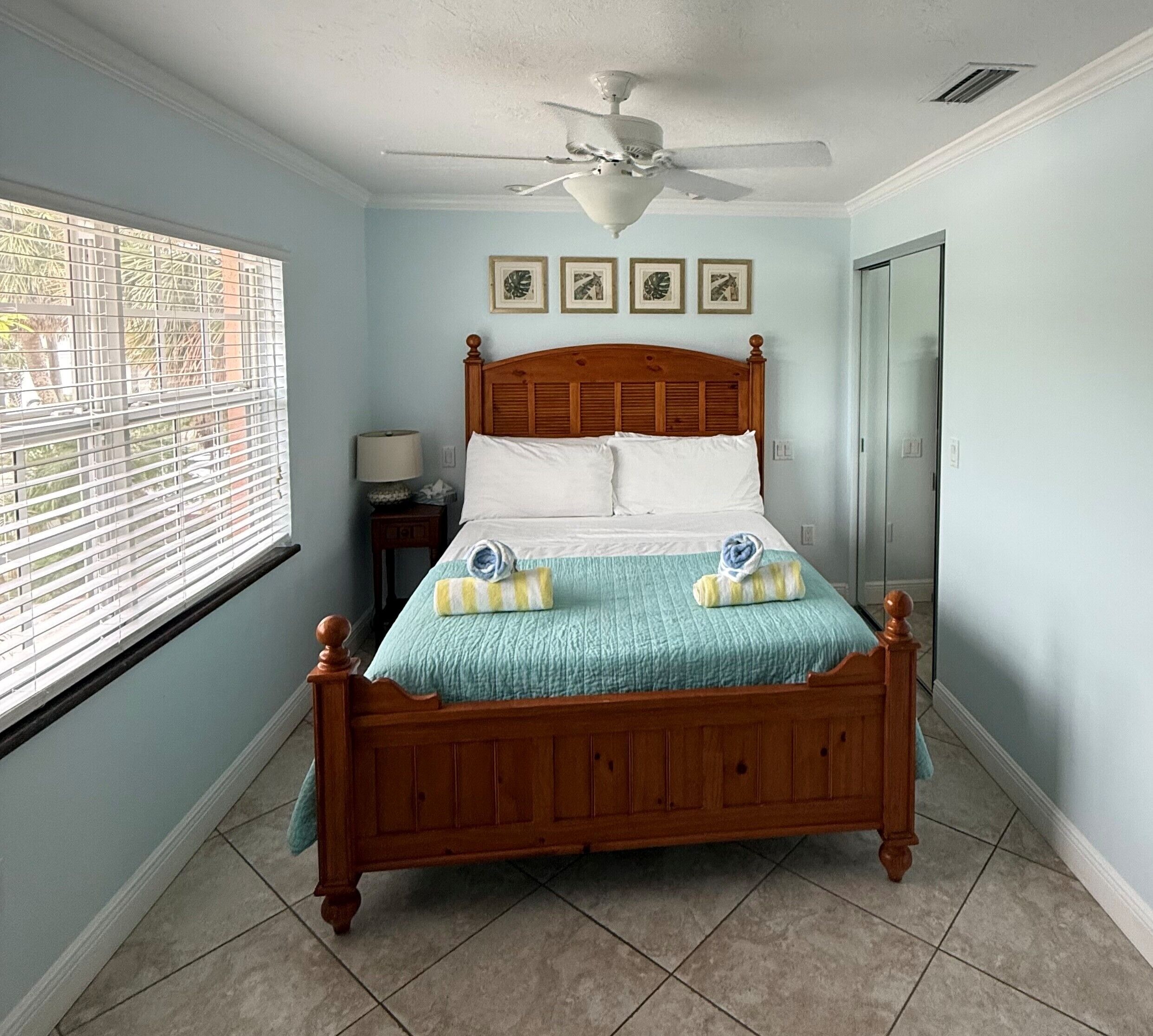 A bedroom with a wooden bed, a ceiling fan, and a window with blinds.