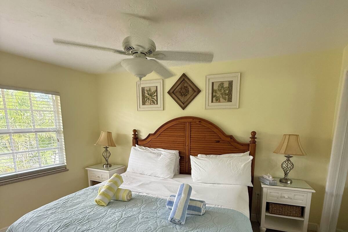 A bedroom with a bed, two nightstands, a ceiling fan, and two wall-mounted pictures.