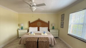 A bedroom with a bed, two nightstands, a ceiling fan, and a window with blinds. - Siesta Key Inn (Siesta Key)