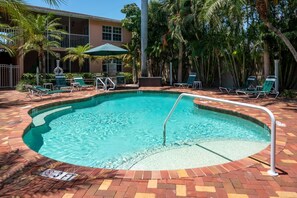 A swimming pool with a brick border, surrounded by lounge chairs and palm trees.