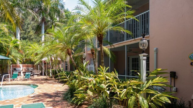 A pool area with lounge chairs, palm trees, and a building with balconies. - Siesta Key Inn (Siesta Key)