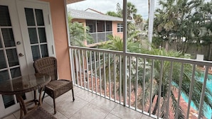 A balcony with wicker furniture, a glass table, and a view of a swimming pool and palm trees. - Siesta Key Inn (Siesta Key)