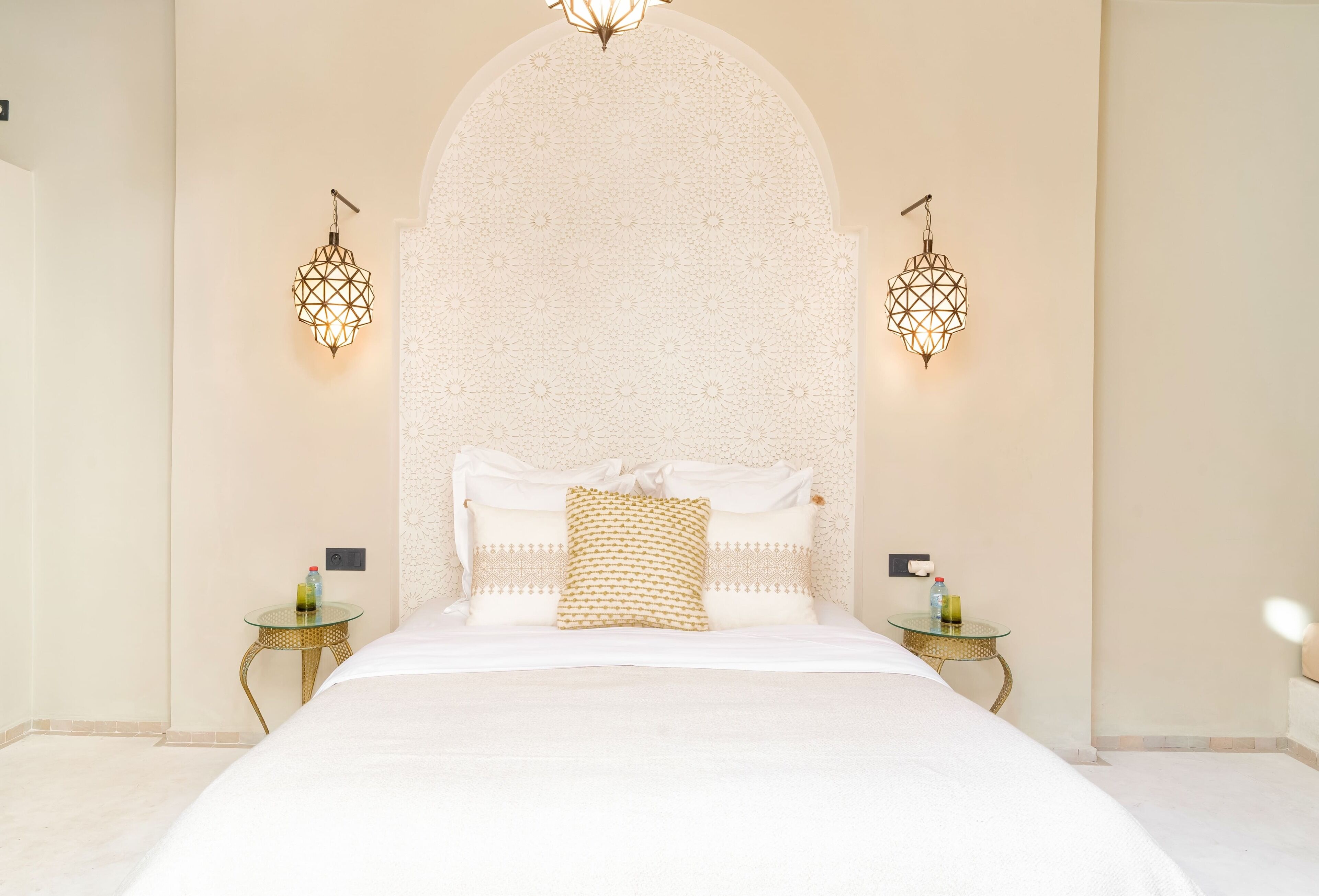 A hotel room with a large bed, two bedside tables, and decorative wall sconces.