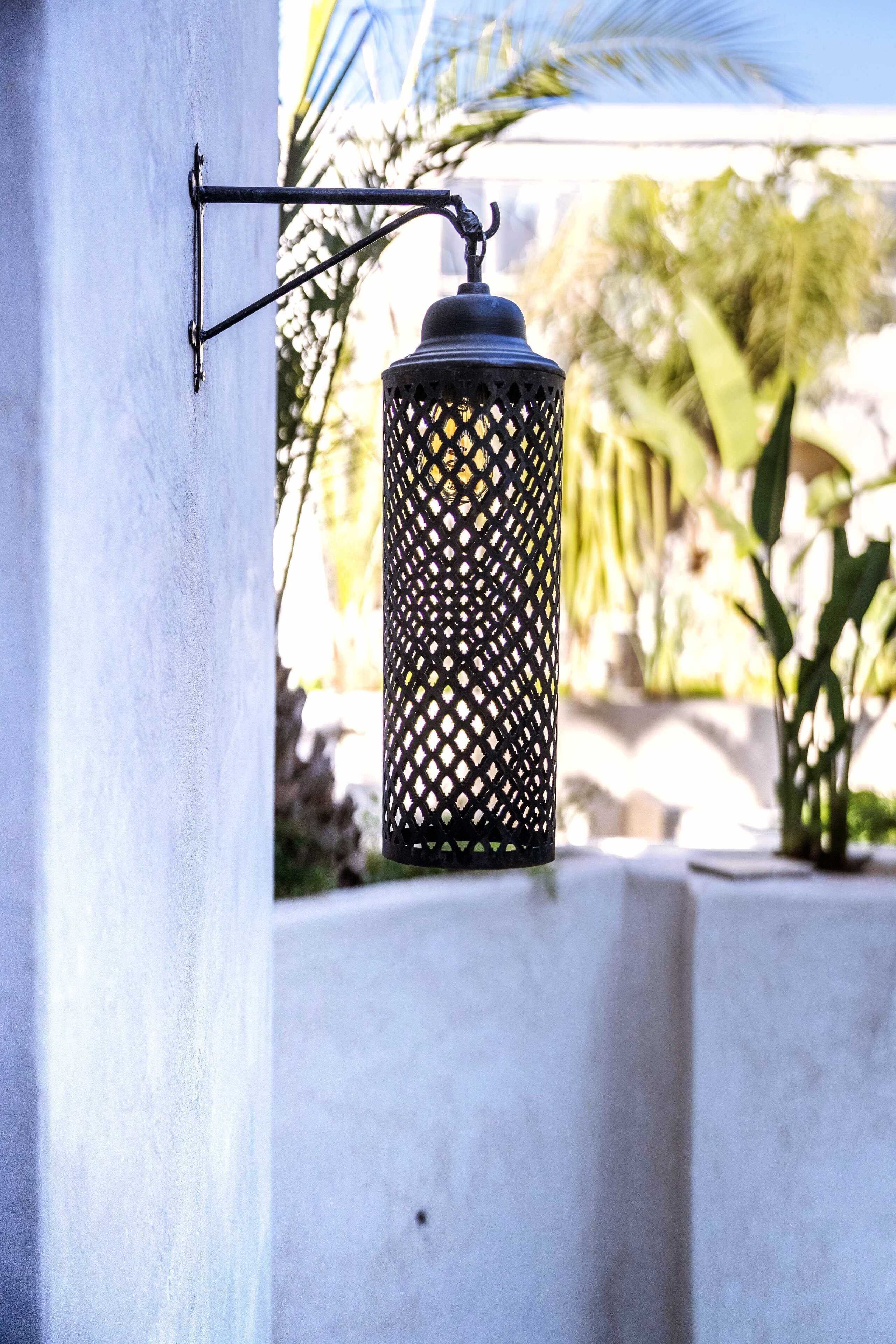 Un farol exterior negro sujeto a una pared, con un diseño de celosía.