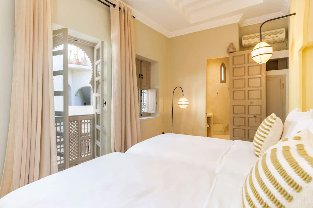 A hotel room with a bed, curtains, a wall-mounted lamp, and a door.