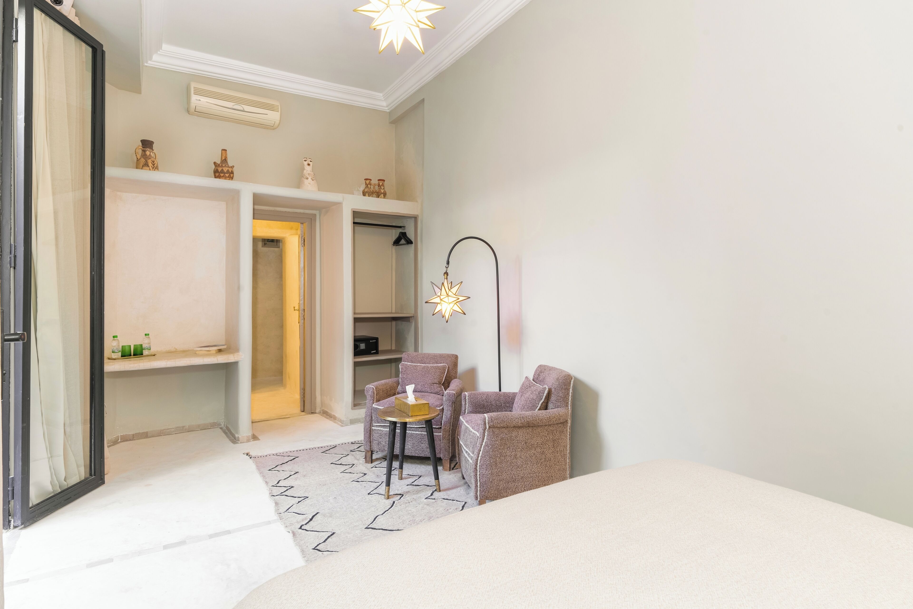 A hotel room with a bed, two armchairs, a small table, a mirror, and a wardrobe.