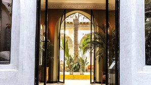 An arched corridor with checkered flooring leading to a courtyard with plants and a view of a building with arches. - RIAD XO (Marrakech)