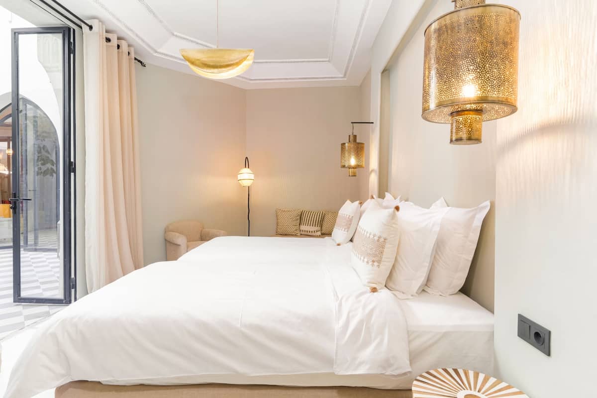 A bedroom with a large bed, a ceiling fan, a floor lamp, and a view of the outside.